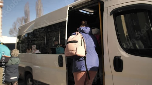 An adult woman in a jacket with a backpack enters a passenger bus.