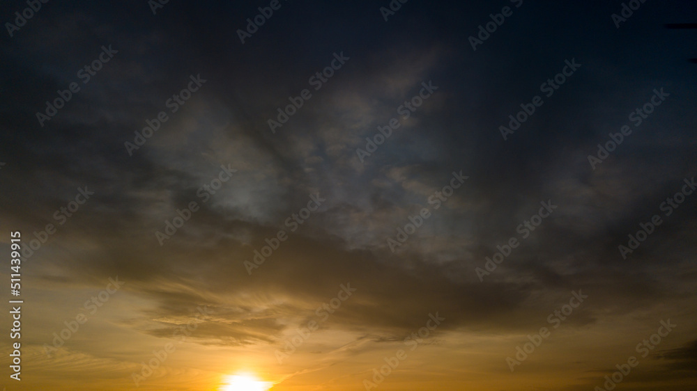 Dramatic sunset landscape with puffy clouds lit by orange setting sun and blue sky Dramatic sunset landscape with puffy clouds lit by orange setting sun and blue sky