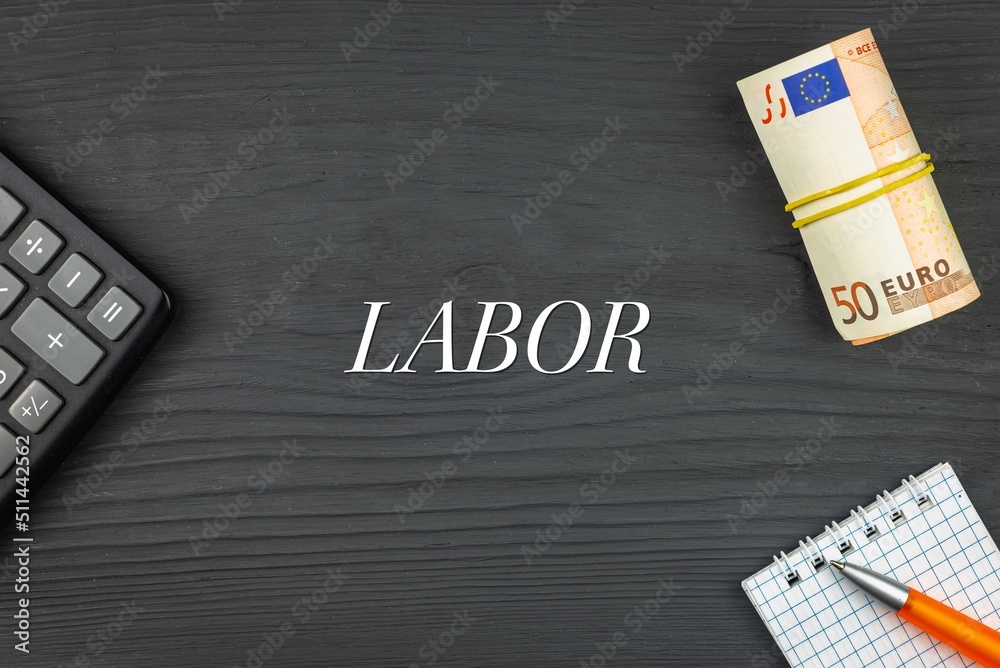 LABOR - word (text) and euro money on a wooden background, calculator, pen and notepad. Business concept (copy space).