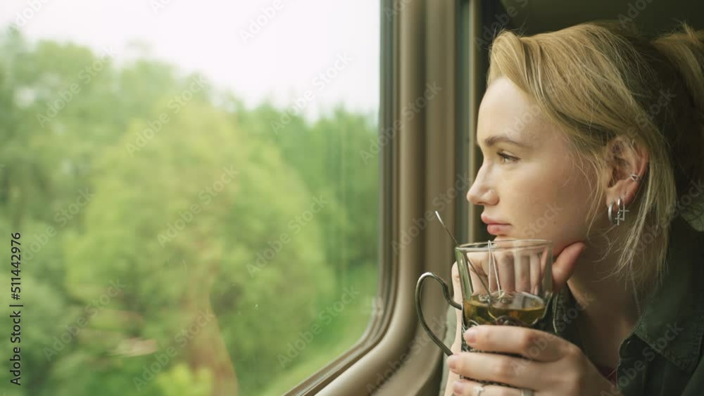 blonde on the train holds a glass of tea in her hands and looks out the window blonde on the train holds a glass of tea in her hands and looks out the window