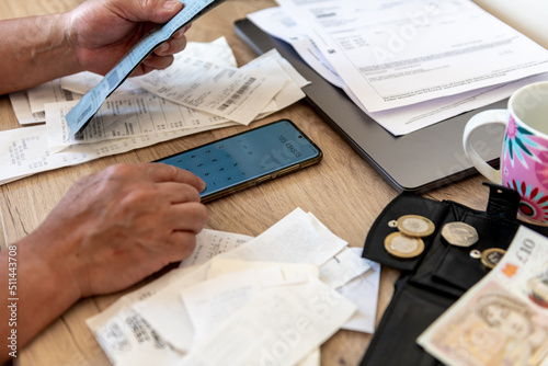 Tablou pe pânză A person calculating the cost of living with a phone calculator and a desk full of bills and till receipts