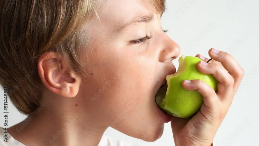 Cute child caucasian boy bites a green apple, chewing over white background. Close-up. Healthy lifestyle and eating habit.