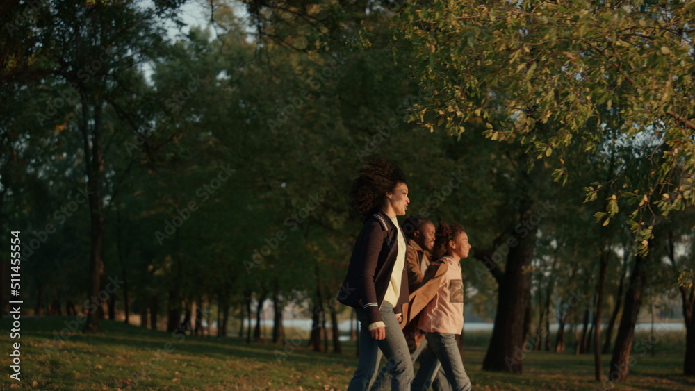 Family walking autumn park holding hands together in evening golden sunlight.