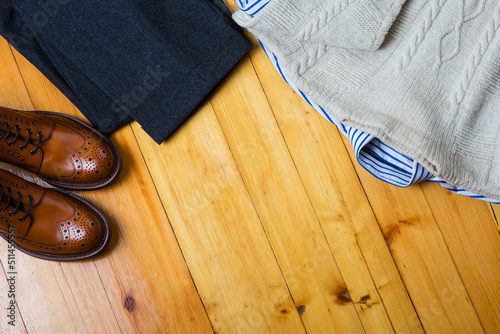 Clothing Concepts. Upper View Flat Lay of Tan Brogues Boots With Winter Sweater, Striped Shirt, Pair of Herringbone Trousers on Wooden Surface Background.