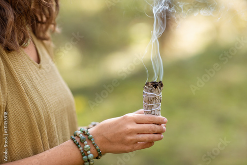 occult science and supernatural concept - close up of woman or witch with smoking white sage performing magic ritual in forest