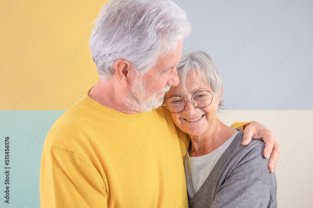 Lovely attractive caucasian senior couple embracing over isolated colorful background. Elderly white-haired man looking at his wife smiling enjoying good company and free time