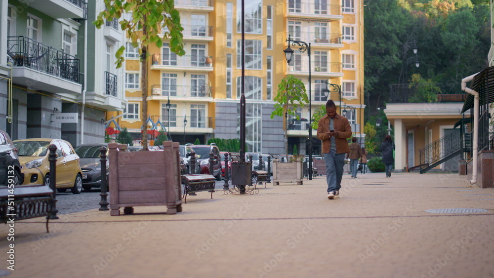 Happy man walking city street using smartphone. Urban traveler wandering around