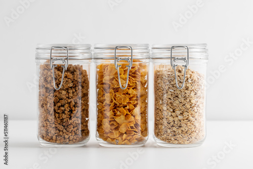 food, healthy eating and diet concept - jars with oat, corn flakes and granola on white background