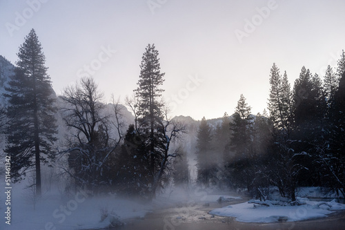 Yosemite valley is enshrouded in a thin layer of mist hanging over the merced river, providing an eerie atmosphere around sunset.