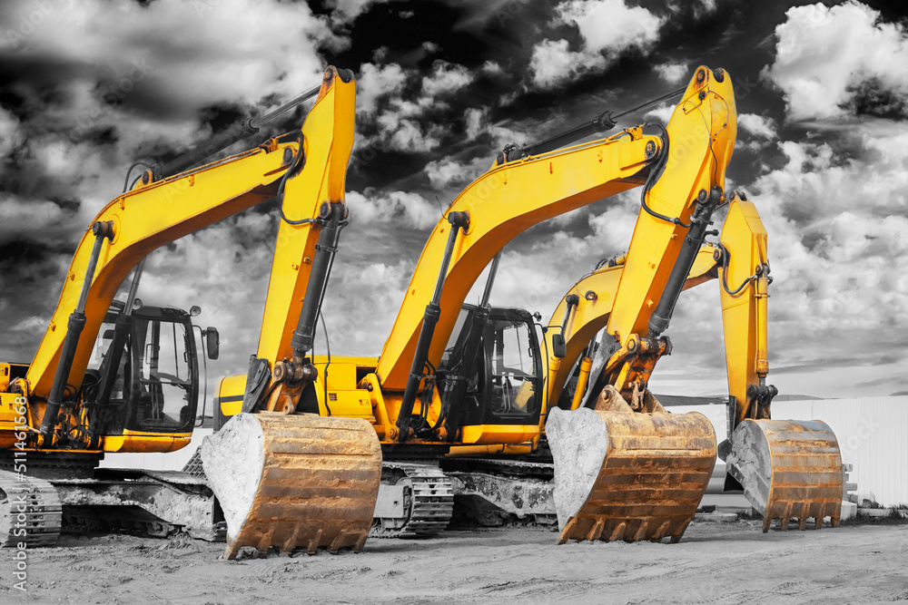 Powerful excavators at a construction site against a cloudy evening sky. earthmoving construction equipment. Lots of excavators.