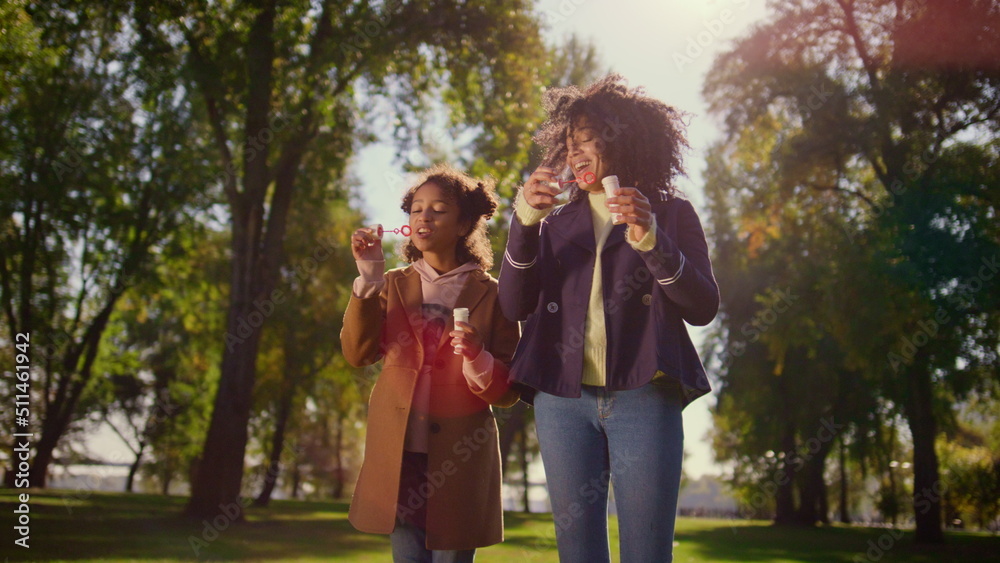 Naklejka premium Joyful family blowing soap bubbles standing in green park. Happy leisure time.