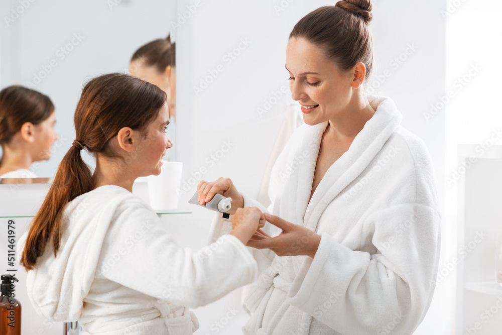 beauty, hygiene, morning and people concept - happy smiling mother and daughter applying toothpaste to toothbrush at bathroom beauty, hygiene, morning and people concept - happy smiling mother and daughter applying toothpaste to toothbrush at bathroom