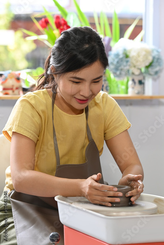 Young creative woman working with clay, creating handicrafter ceramic on the pottery wheel in art workshop. Pottery working, handmade clay products photo
