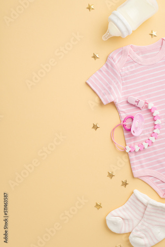 Baby accessories concept. Top view vertical photo of infant clothes pink bodysuit tiny socks bottle pacifier chain and gold stars on isolated pastel beige background