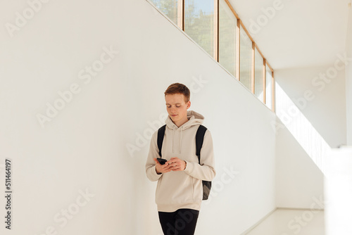 Male student walking in university corridor. Young man with smartphone in college.