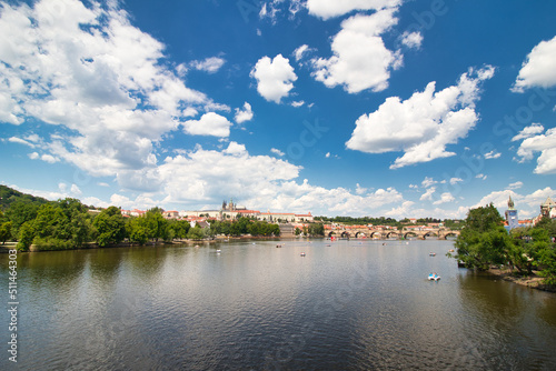 Look over Vltava river to Charles bridge  Prague Castle in background under blus sky with white clouds.