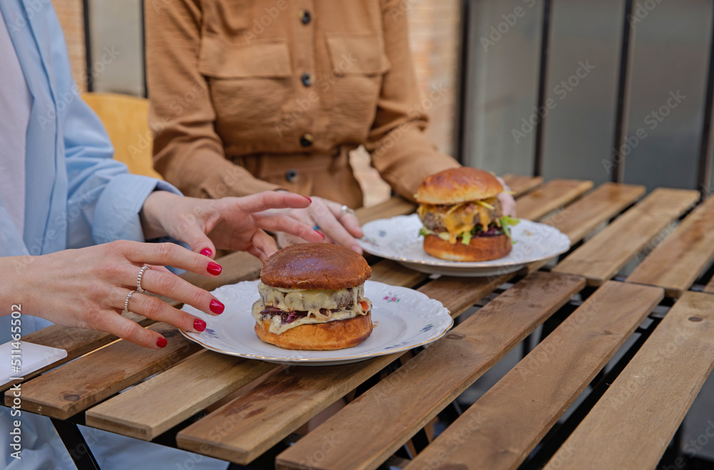 Girlfriends in the restaurant and juicy burgers in their plates. Eat burgers in a good company of like-minded people. Girls are ready to eat delicious burgers. Lunch with a friend