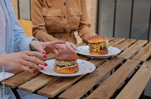 Obraz na płótnie Girlfriends in the restaurant and juicy burgers in their plates. Eat burgers in a good company of like-minded people. Girls are ready to eat delicious burgers. Lunch with a friend w salonie