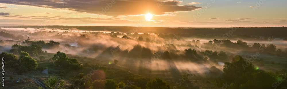 Sunrise of meadow with forest in sunlight and mist