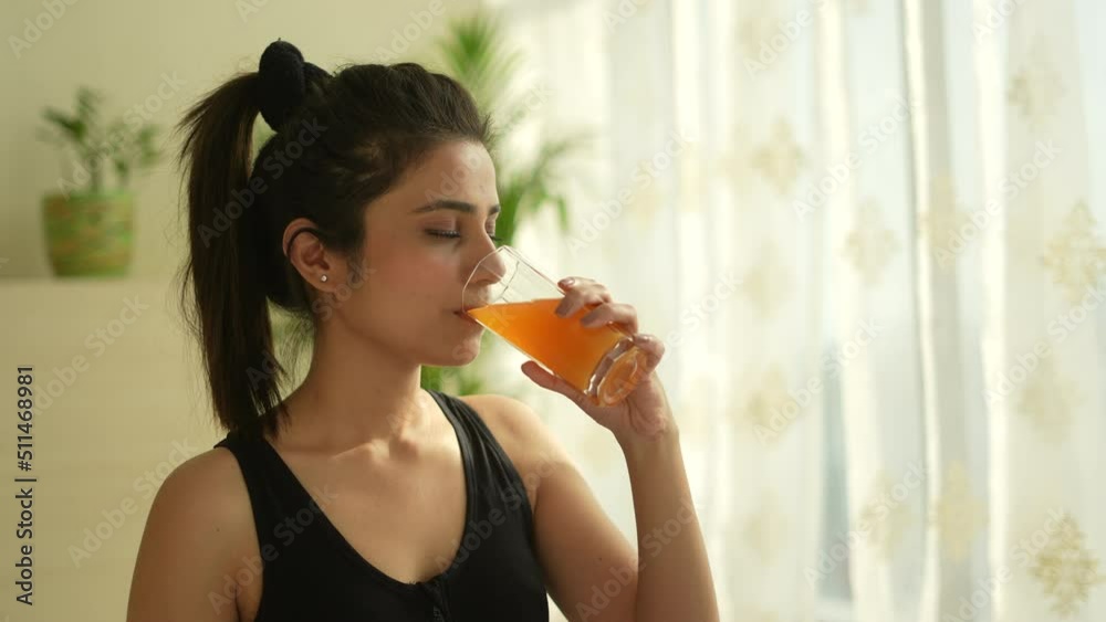 A Beautiful indian woman driking mixed orange juice after yoga.Asian woman doing yoga on yoga met.looking other side  