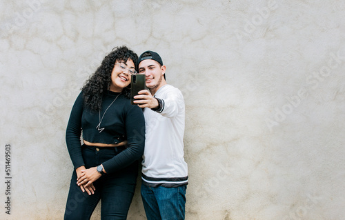 Young couple taking a selfie near a wall with copy space, Young friends taking a selfie leaning against a wall, Young happy couple taking a selfie leaning against a wall