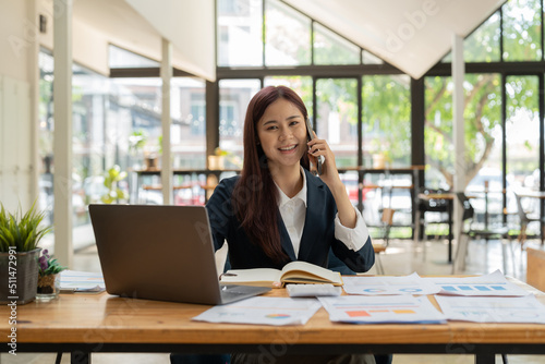 Smiling business asian woman in black suit talking on phone