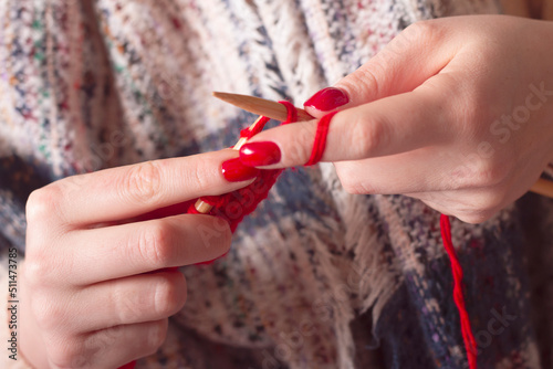 The girl knits with knitting needles from red threads. Women's hands close-up