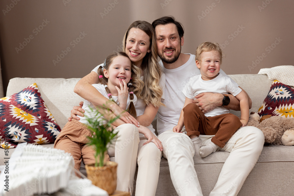 Big happy family. Portrait of mother father and their two sweet children, a sister and brother, sitting together on a sofa at home and smiling for the camera. Mortgage and real estate moving concept.