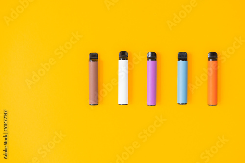 Layout of colorful disposable electronic cigarettes with shadows on a yellow background. The concept of modern smoking  vaping and nicotine. Top view