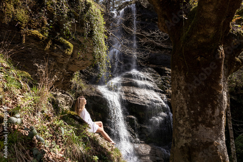 woman sitting on a waterfall in a white dress