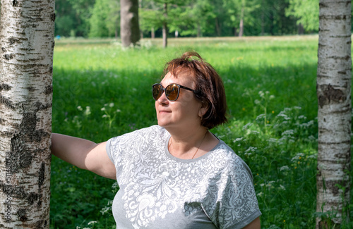 Portrait of a happy attractive mature woman 50-60 years old on a blurry green background near birches, travel and retirement