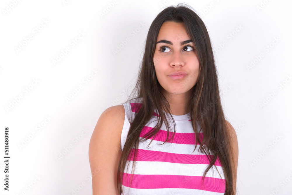 young beautiful brunette woman wearing striped top over white wall, looks pensively aside, plans actions after university, imagines what to do Thinks over about new project. young beautiful brunette woman wearing striped top over white wall, looks pensively aside, plans actions after university, imagines what to do Thinks over about new project.