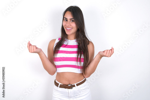 young beautiful brunette woman wearing striped top over white wall, making money gesture. © Jihan