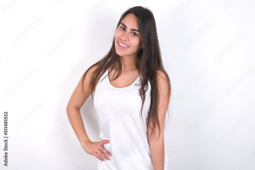 Studio shot of cheerful Young beautiful brunette woman wearing white top over white wall keeps hand on hip, smiles broadly. Studio shot of cheerful Young beautiful brunette woman wearing white top over white wall keeps hand on hip, smiles broadly.