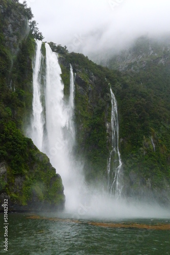 Turbulent waterfalls falling from foggy mountain and striking the peaceful water with wonderful spray at Milford Sound  New Zealand