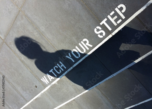 Watch your step marking on the ground with shadow of a walking lady
