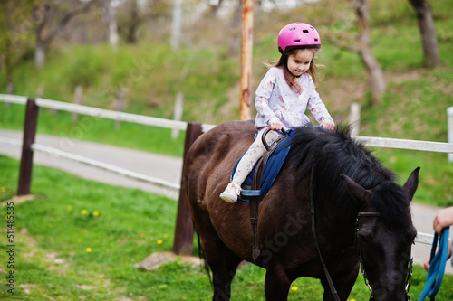 Small baby girl in pink helmet ride pony.