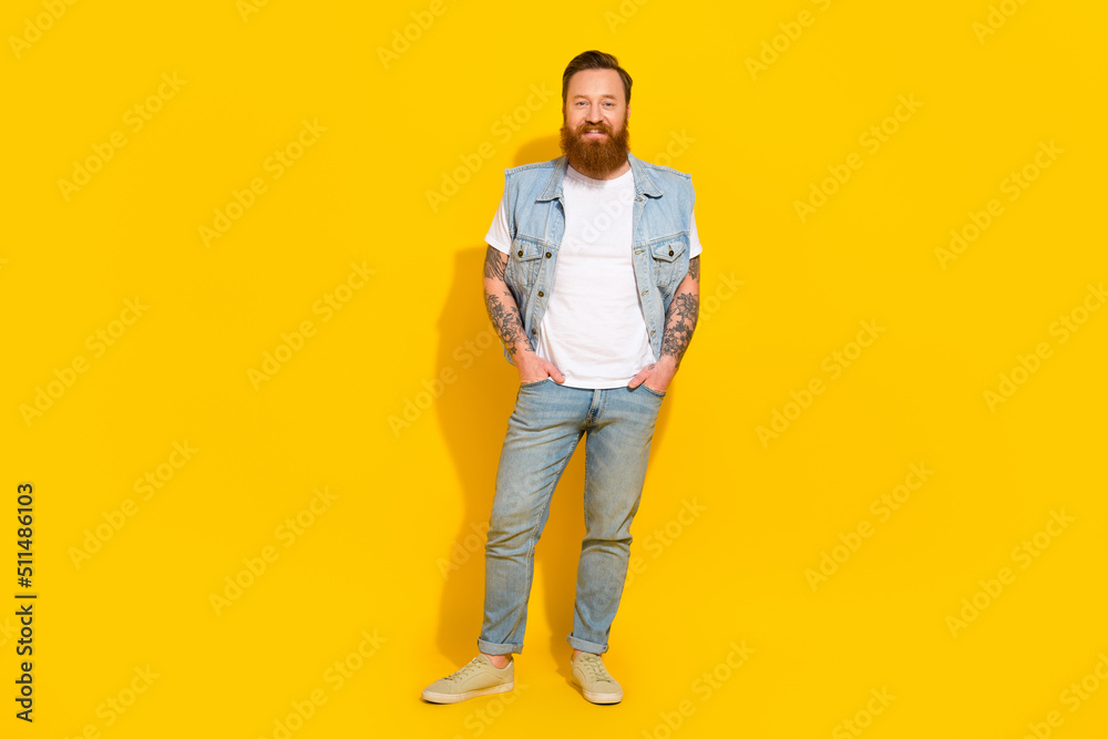 Photo of funky pretty man wear jeans waistcoat arms pockets walking empty space isolated yellow color background Photo of funky pretty man wear jeans waistcoat arms pockets walking empty space isolated yellow color background
