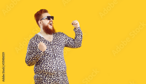 Crazy happy funny bearded fat man laughs out loud and sincerely rejoices in his success and triumph. Joyful man in leopard clothes happily clenched his fists and shouts cheers on orange background. photo