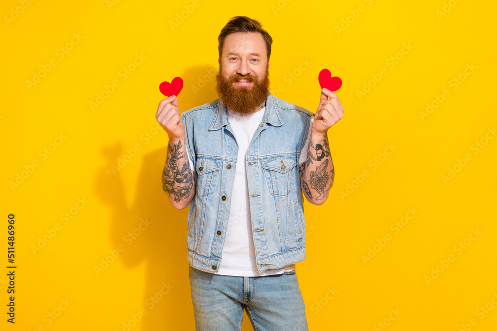 Portrait of satisfied glad man hold two little heart figure postcards isolated on yellow color background Portrait of satisfied glad man hold two little heart figure postcards isolated on yellow color background