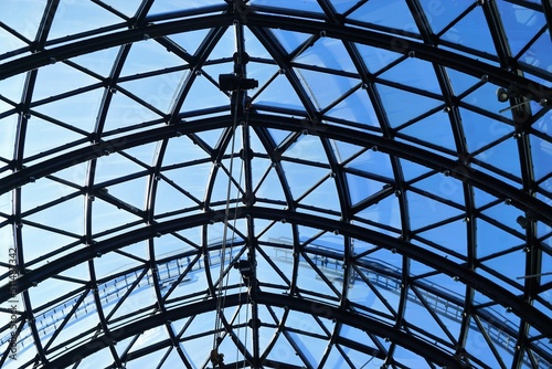 Glasdach mit Rundbogengitter aus schwarzem Stahl vor blauem Himmel bei Sonne im Frühling