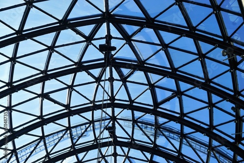 Glasdach mit Rundbögen aus schwarzem Stahl vor blauem Himmel bei Sonne im Frühling 