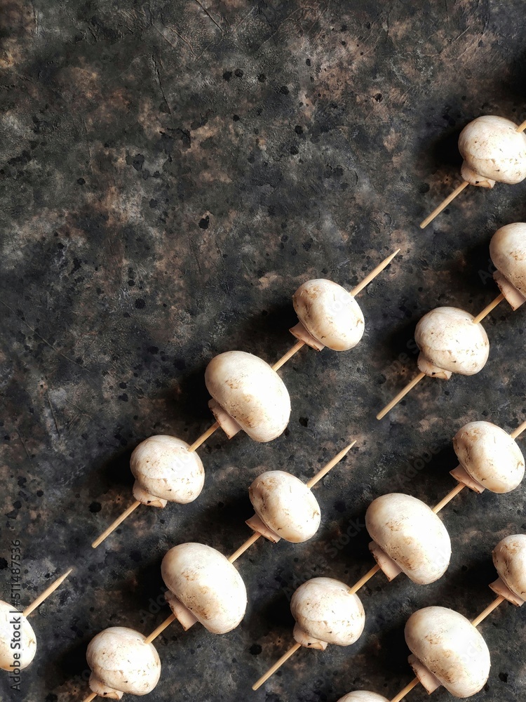 Background of champignons on a wooden skewer Mushroom pattern on a black concrete background with copy space. Vegetables to replace meat.