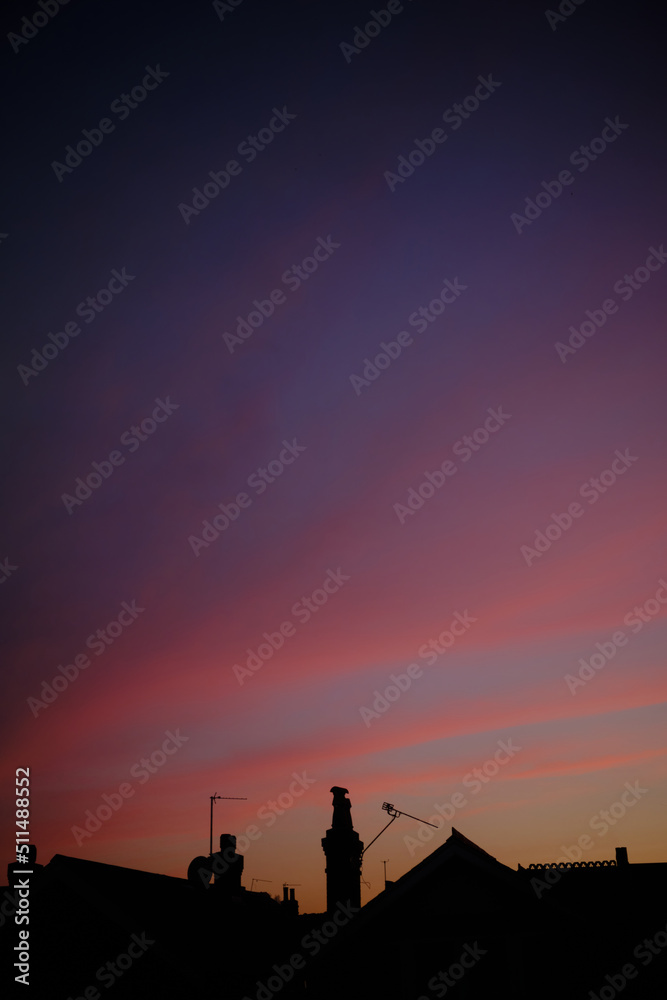 Rooftops silhouetted against a vibrant purple and blue sunset sky.