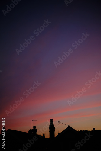 Rooftops silhouetted against a vibrant purple and blue sunset sky.