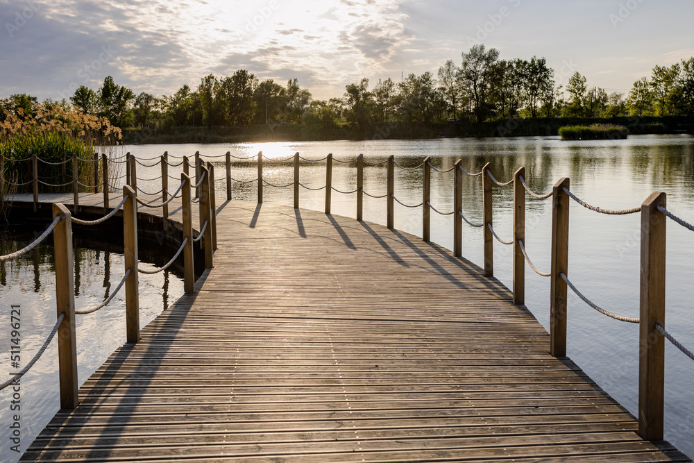 Fototapeta premium Long Wooden bridge over lake. Beautiful sunrise over lake pier. Planked footway on the river