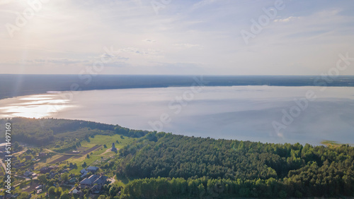 Aerial view of lake and small village on the peninsula. Sunset evening light by calm water on warm beautiful summer day.