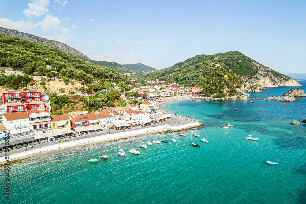 Beautiful colorful houses of seaside town of Parga with boats, cruise ship. Sand beach with umbrellas, tourist people, blue, turquoise sea water. Summer vacations and travel concept. Greece. 