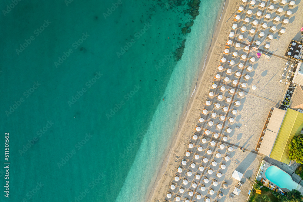 Aerial view of many white sunbed, lounge, umbrellas on sandy beach. Summer and travel concept. Blue, turquoise transparent water surface of ocean, sea, lagoon. Aerial, drone view