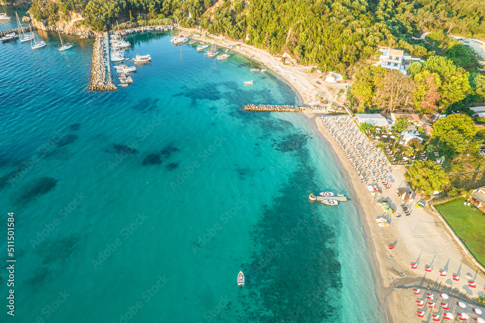 Port with boats, cruise ship and colorful houses of seaside town of Parga. Beach with tourist people, blue, turquoise sea water. Summer vacations and travel concept. Greece. Aerial, drone view